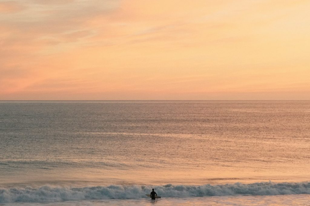 A surfer enjoys the calm ocean at sunset.